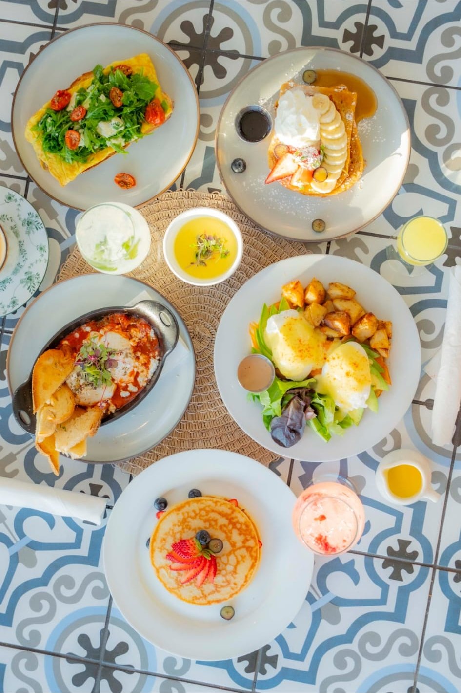 Overhead brunch spread — arepas, eggs, coffee, mimosas — shared across a warm oak table.